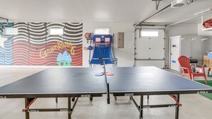 Ein Tischtennis-Tisch mit Netz in der Mitte, ein blauer Stuhl und eine Wand mit einem farbenfrohen Wandgemälde.