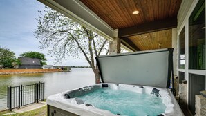 Ein Whirlpool mit Holzboden und Steinwänden, mit Blick auf ein Gewässer und eine Rasenfläche.