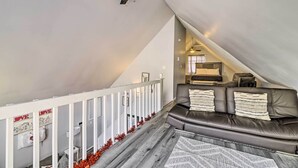 A modern loft bedroom with a sloped ceiling, a dark leather sofa, and a white railing along the staircase. - Tobyhanna Home Near Kalahari w/ Lake & Pool Access (Tobyhanna)
