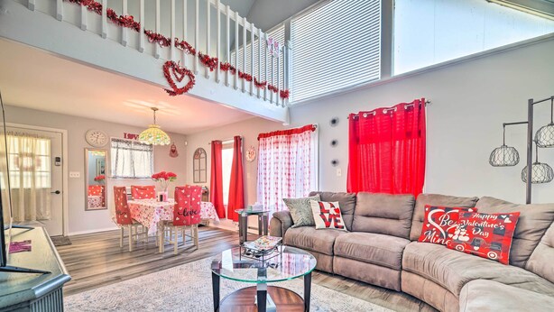 A living room with a glass coffee table, a brown sofa, red curtains, and a dining area with a red tablecloth. - Tobyhanna Home Near Kalahari w/ Lake & Pool Access (Tobyhanna)