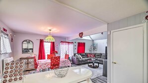 A compact living space with a kitchenette, a dining area with a table and chairs, a sofa, and a large window with red curtains. - Tobyhanna Home Near Kalahari w/ Lake & Pool Access (Tobyhanna)