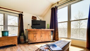 A cozy room with a wooden bench, a television on a wooden stand, and a large window with curtains. - Cozy Lewisburg Getaway w/ Deck + Lake Access! (Lewisburg)