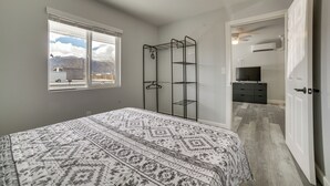 A bedroom with a bed, a walk-in closet, a TV, and a window with a mountain view.