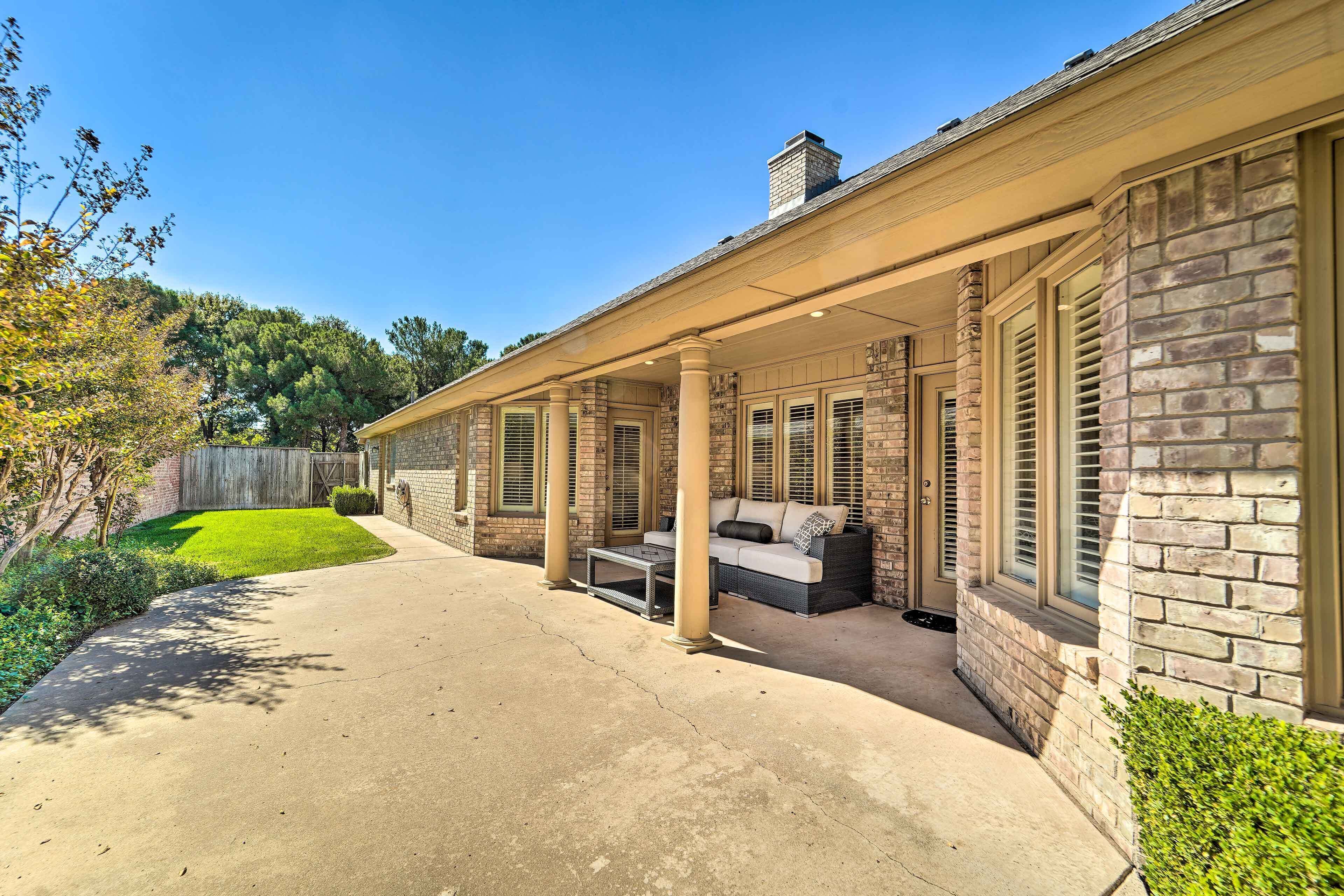 A covered patio with outdoor furniture, a concrete walkway, and a brick house.