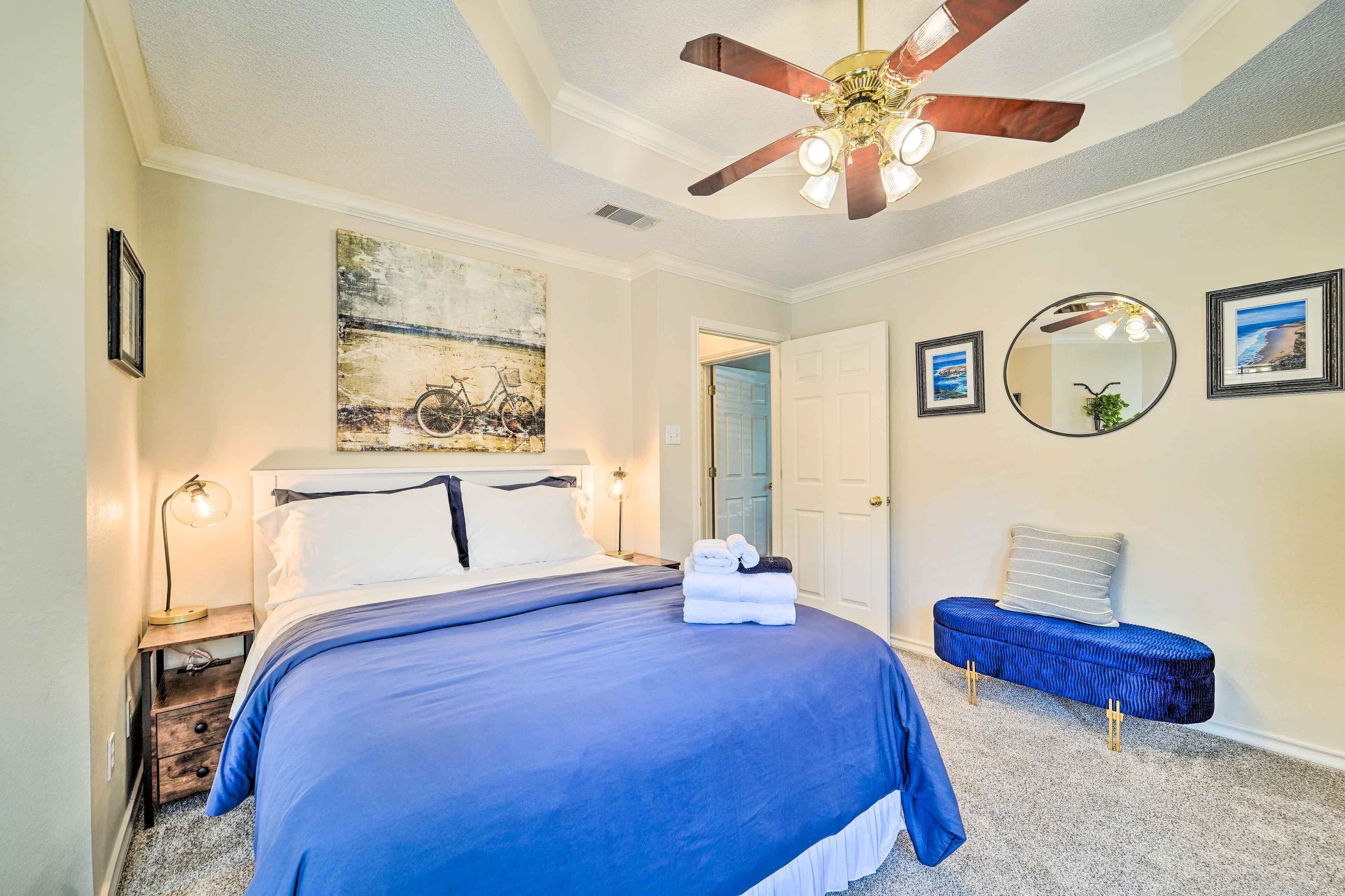 A bedroom with a bed, a ceiling fan, a nightstand, a bench, and artwork on the walls.