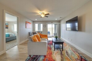 A spacious living area with a ceiling fan, a large flat-screen TV mounted on the wall, and a colorful area rug.