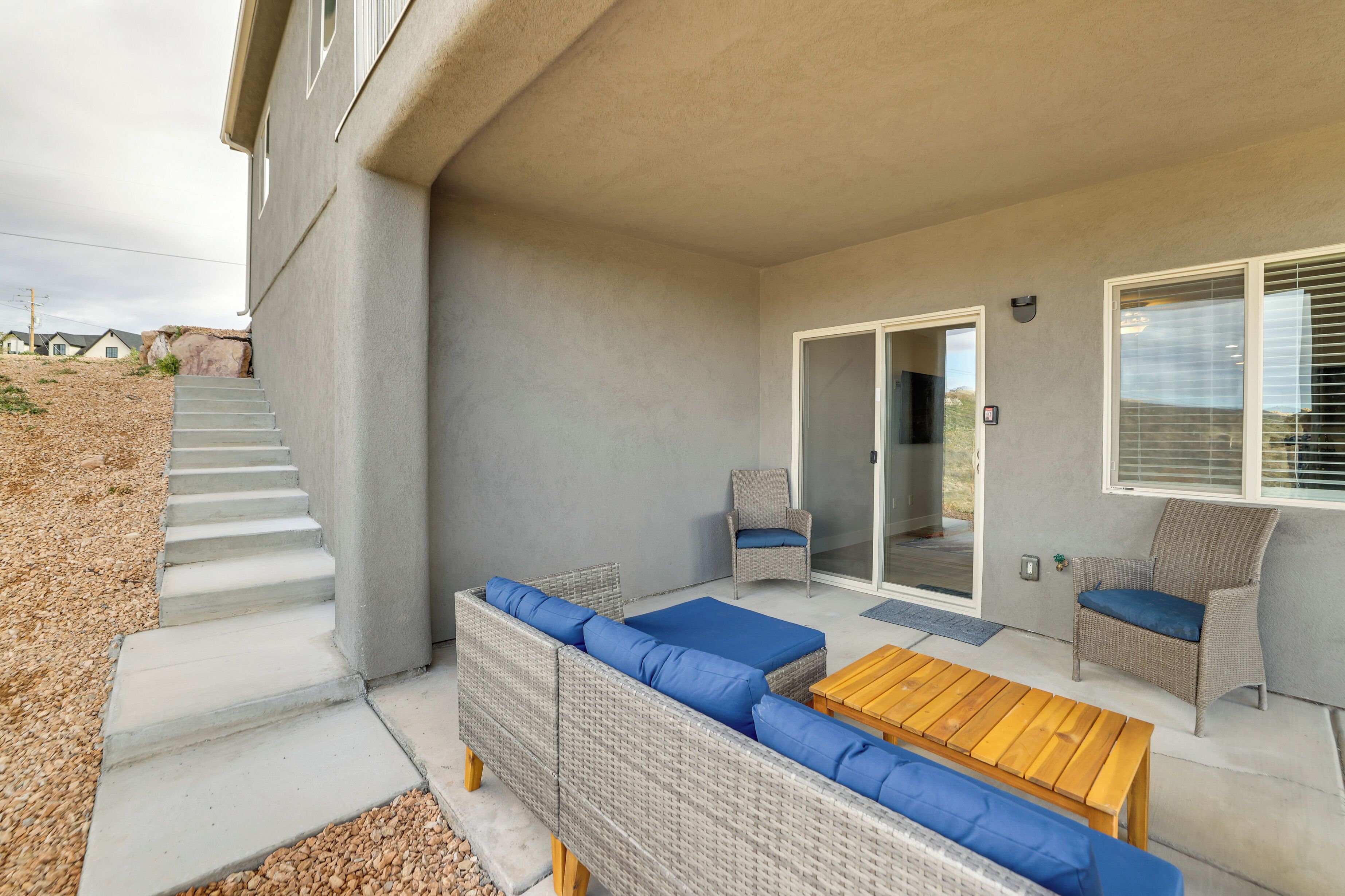 A covered patio area with a wicker sofa set, a wooden table, and two chairs.