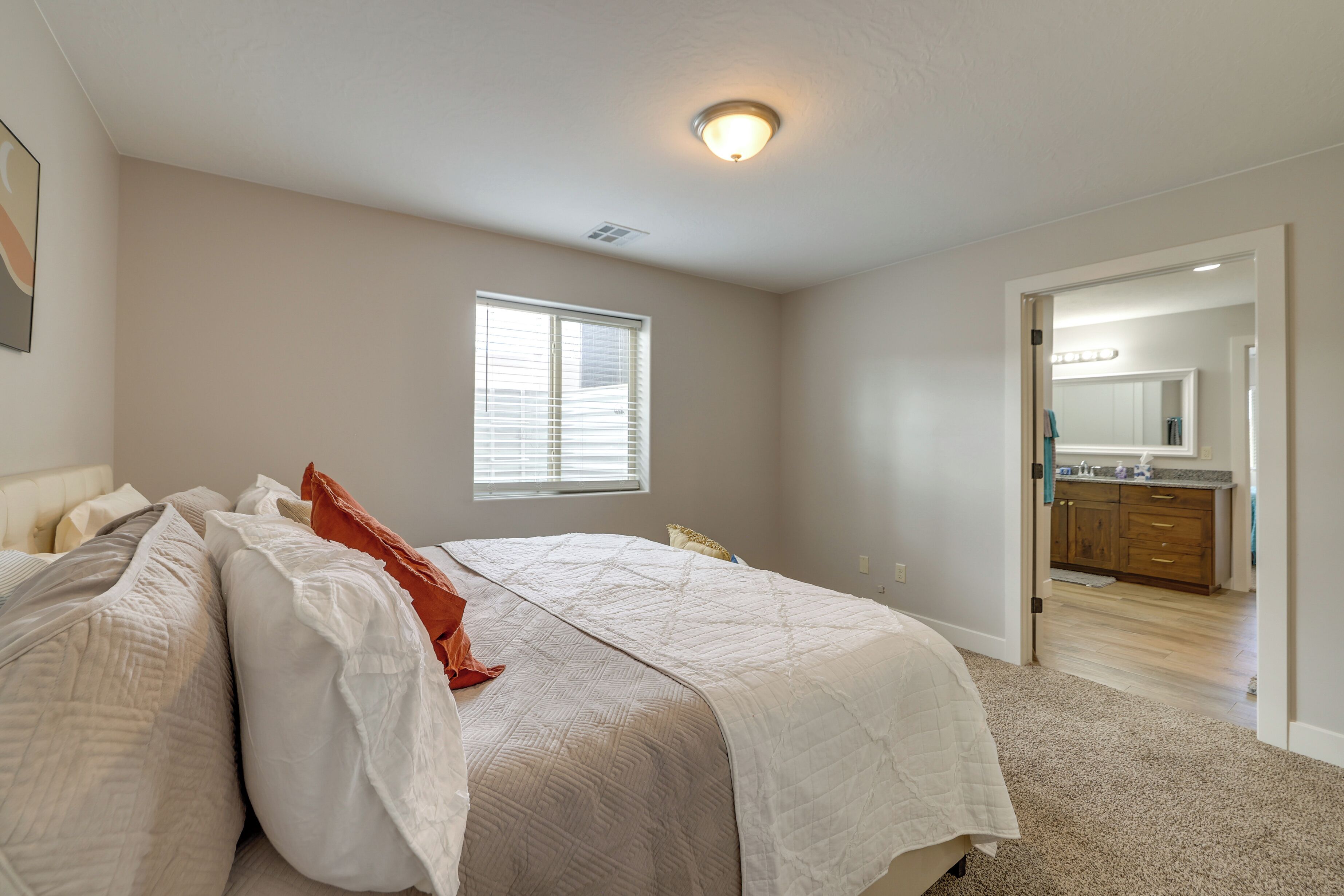 A bedroom with a large bed, a window, and a view into the bathroom.