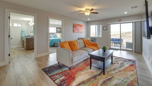 A spacious living room with a sofa, coffee table, and a colorful rug. There is a sliding glass door leading to a balcony with a view. - Toquerville Vacation Rental, Near State Parks! (Toquerville)
