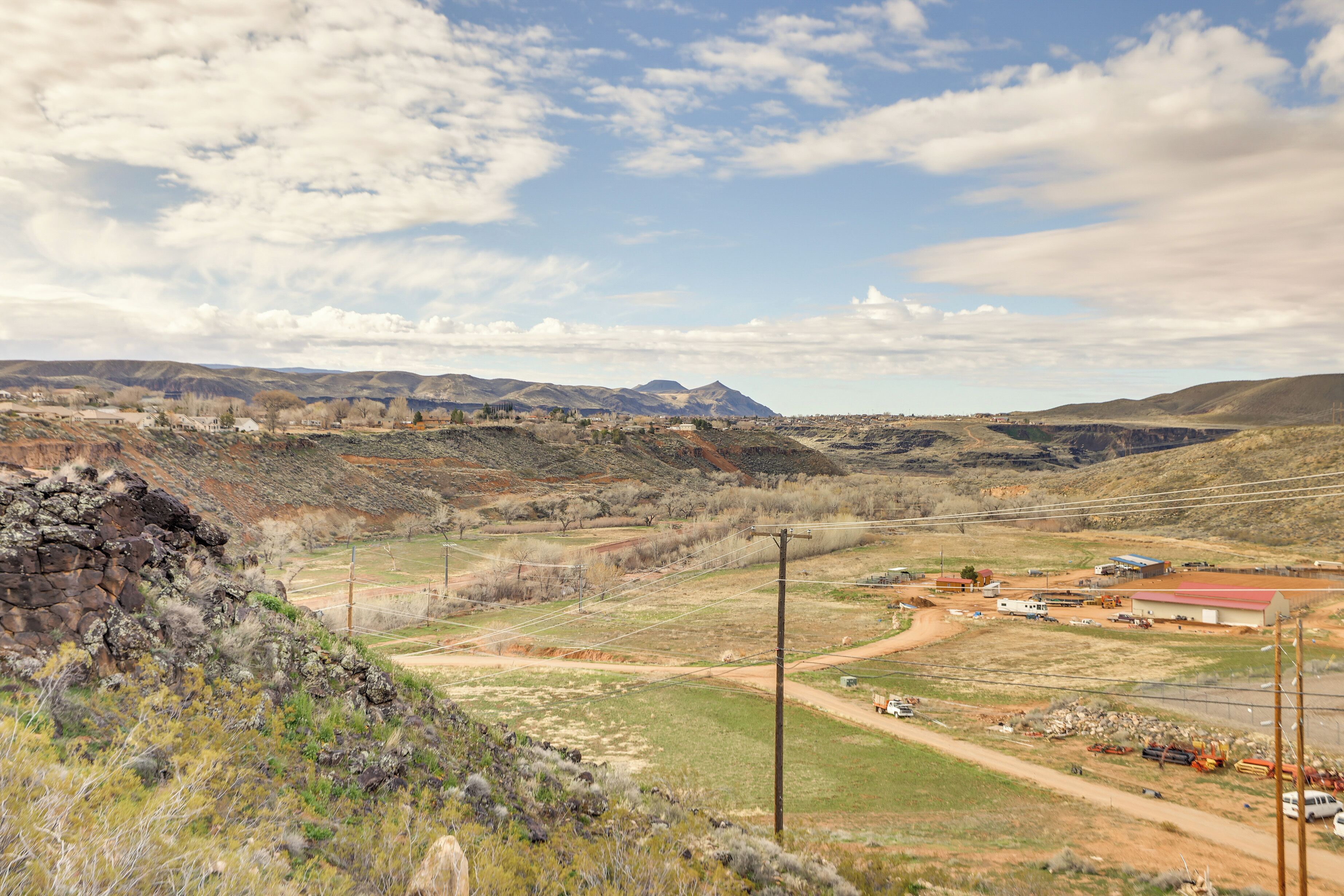 A rural landscape with mountains, a dirt road, and scattered buildings.