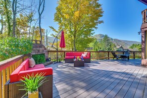 Eine Holzterrasse mit Sitzgelegenheiten im Freien, einem Kamin aus Stein und Blick auf Berge.