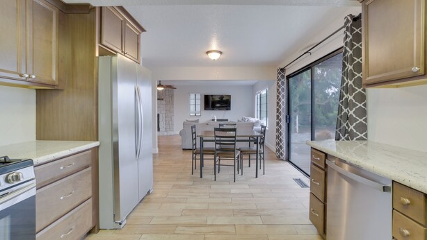 Eine moderne Küche mit Holzausstattung, einem Edelstahlkühlschrank, einem Essbereich mit Tisch und Stühlen sowie einem großen Fenster mit Aussicht.