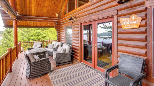 A log cabin with a wooden deck, outdoor seating area, and a sign welcoming guests. - Rustic Gotham Bay Cabin on Lake Coeur D'alene (Harrison)