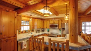 A wooden cabin-style kitchen with a central island, wooden cabinets, stainless steel appliances, and pendant lighting. - Rustic Gotham Bay Cabin on Lake Coeur D'alene (Harrison)