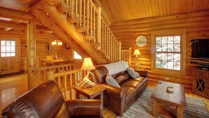A log cabin interior with a staircase, leather furniture, a dining area, and a television. - Rustic Gotham Bay Cabin on Lake Coeur D'alene (Harrison)