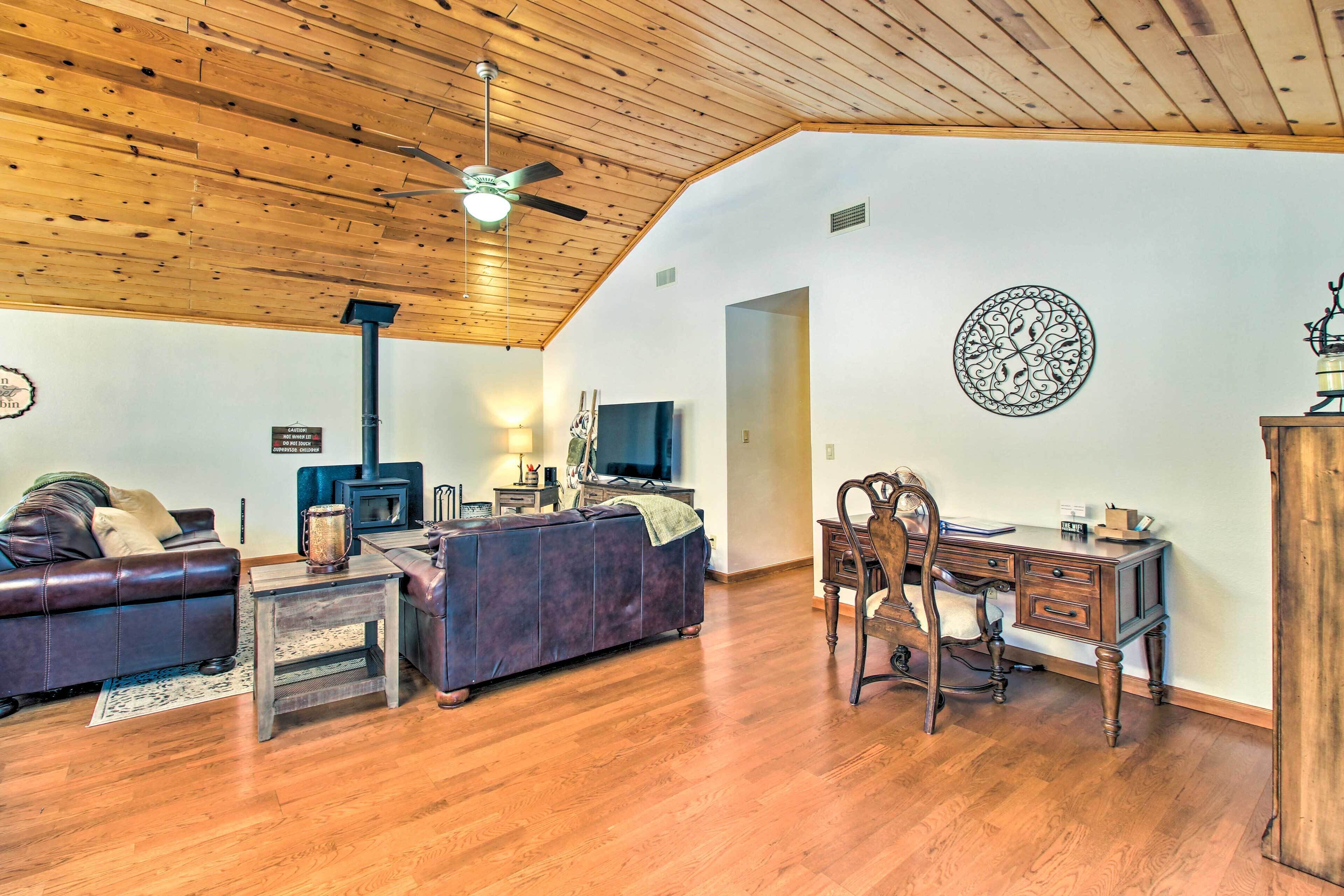 A living room with a wooden ceiling, a fireplace, a sofa, a TV, and a desk with a chair.