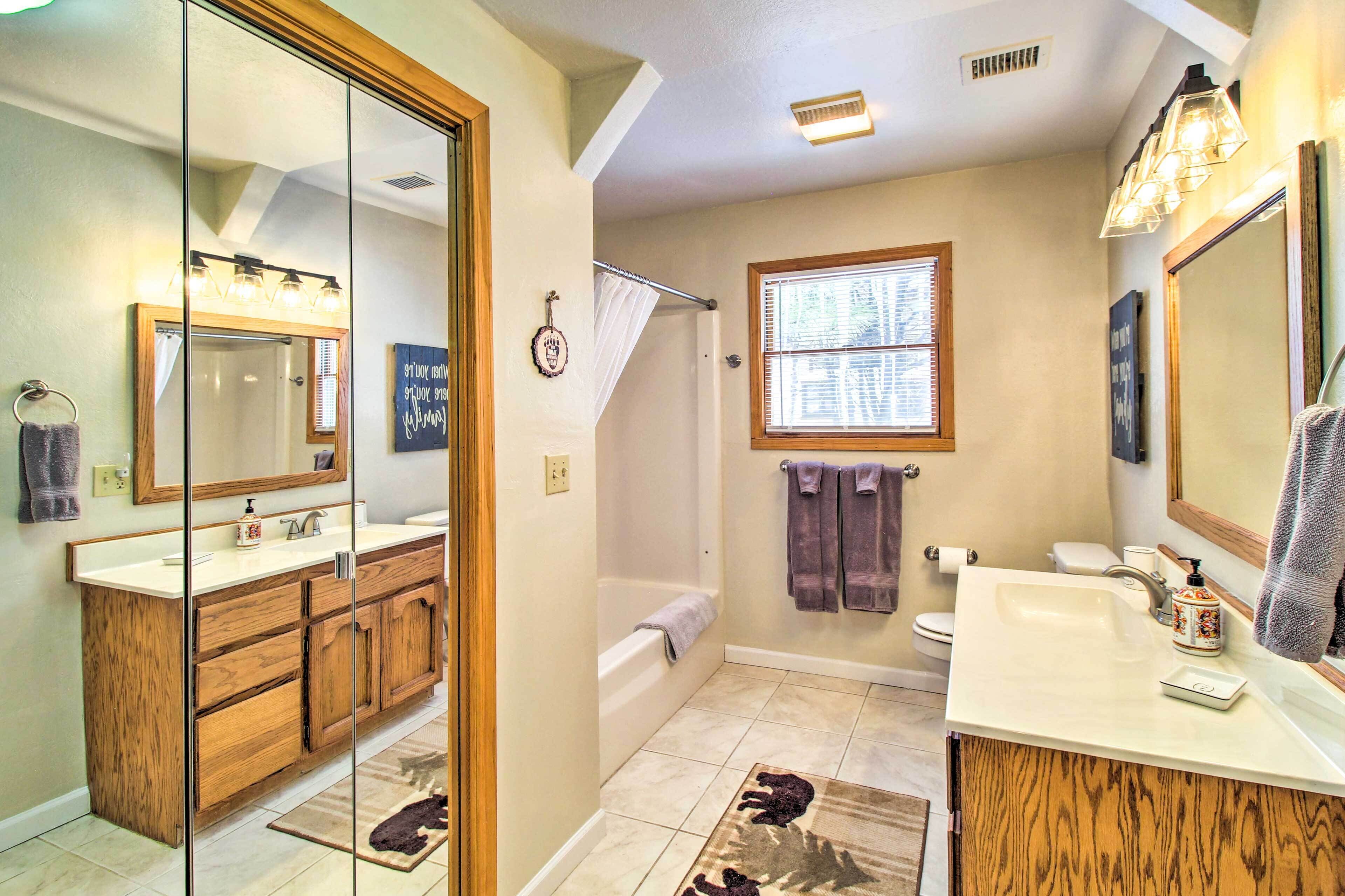 A bathroom with a wooden vanity, a bathtub, a window, and a mirror.