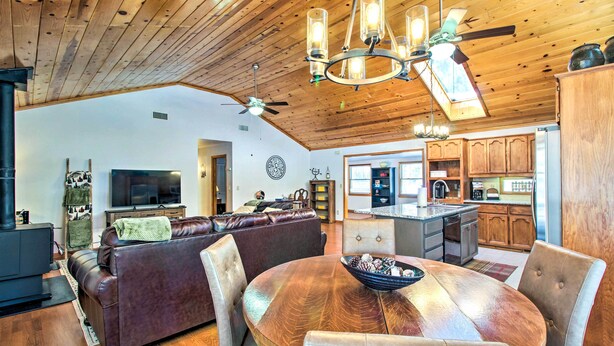A spacious living room with a fireplace, a large leather sofa, a dining table with chairs, and a kitchen area with wooden cabinets and a countertop. - Pet-friendly Cabin in Pinetop-lakeside! (Pinetop)