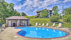 A swimming pool with lounge chairs and a small building, surrounded by greenery and a hill in the background. - Family-friendly Branson Condo w/ Golf Course Views (Branson West)
