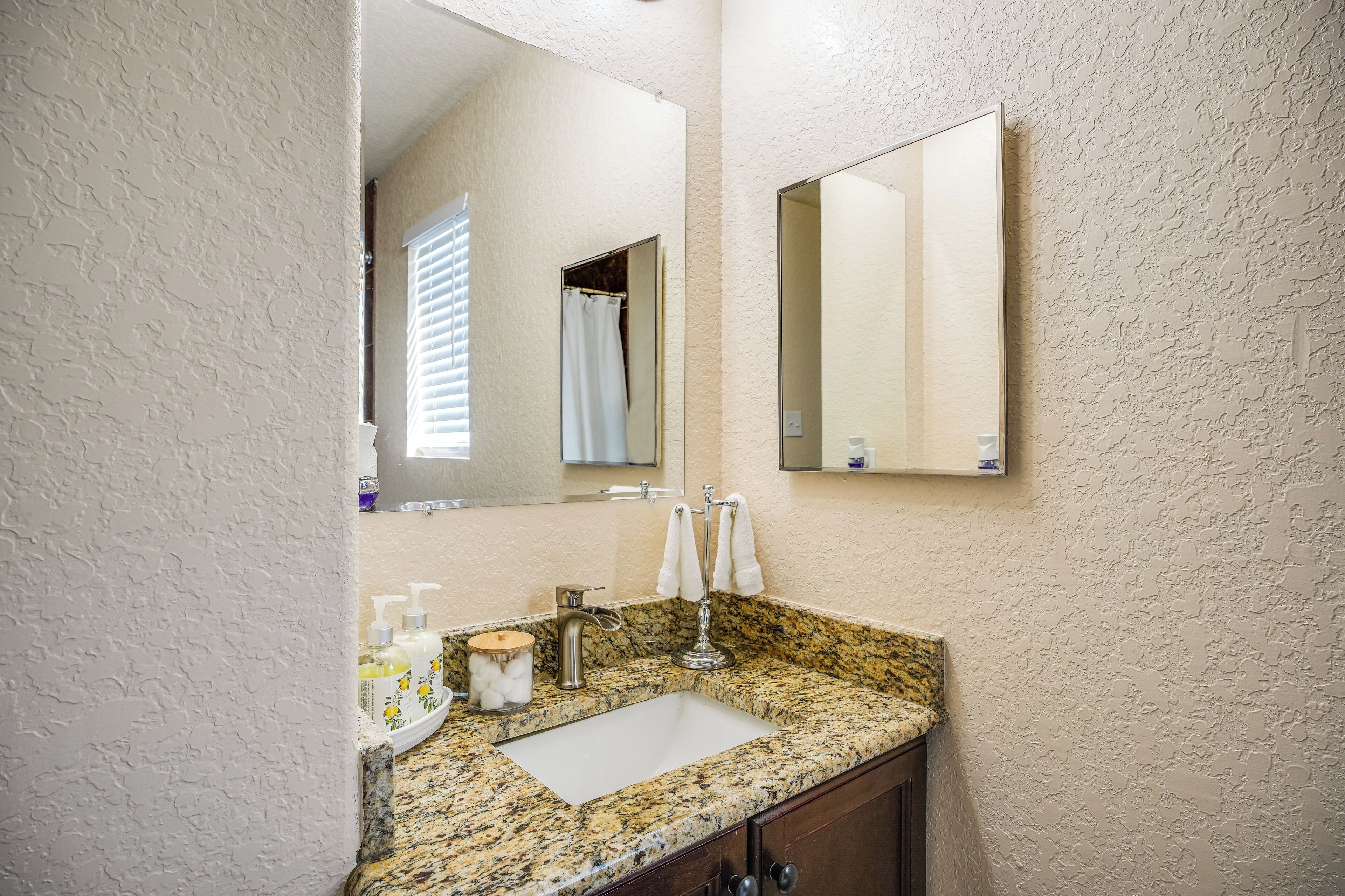 A bathroom with a granite countertop sink, a large mirror, and a towel rack.