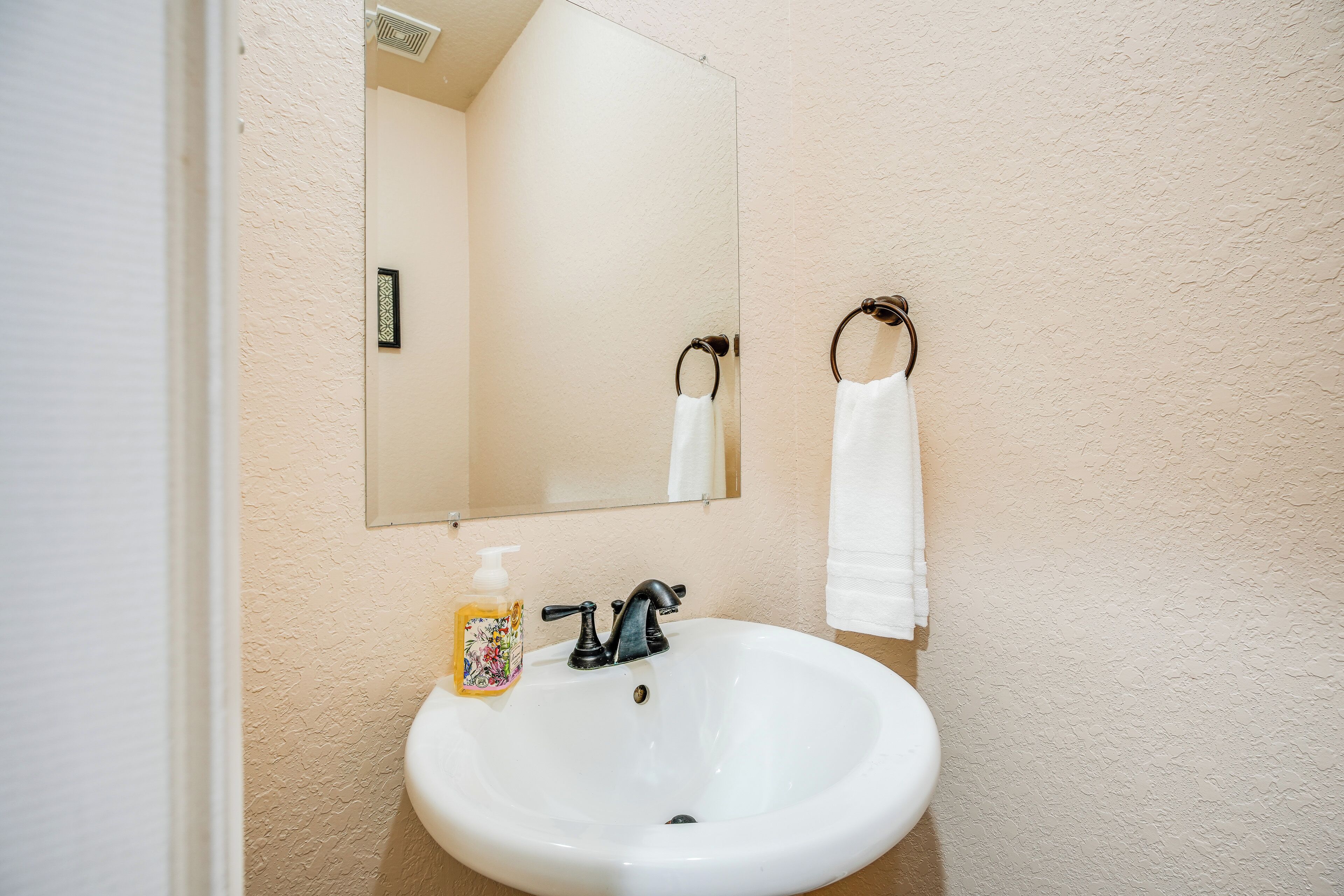 Un baño con lavamanos blanco, un espejo y un perchero para toallas.