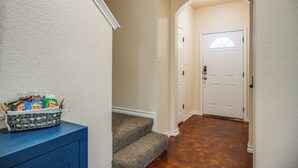 A hallway with a carpeted staircase, a white door with a window, and a basket of beverages on a blue cabinet. - San Antonio Townhome ~ 2 Mi to Aquarium! (San Antonio)