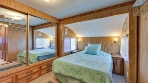 A bedroom with a large mirror, a bed with a green bedspread, wooden walls, and a small cabinet. - Cozy Yuma Vacation Rental w/ Resort Amenities! (Yuma)