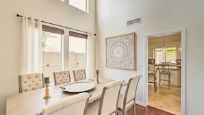 A dining area with a light-colored table, cushioned chairs, and a decorative wall piece. - Golf & Unwind Poolside: Cave Creek Group Retreat! (Cave Creek)