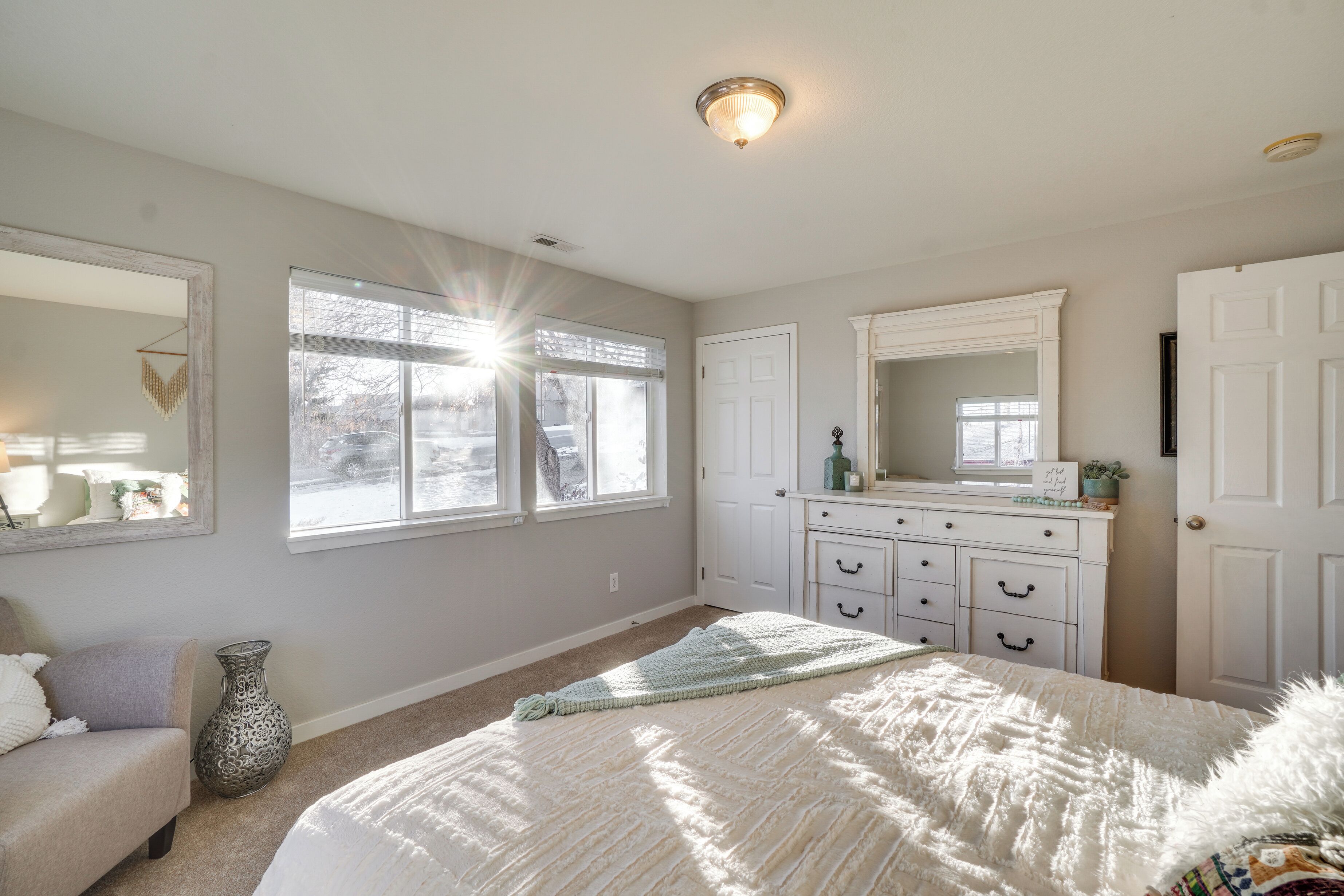 A bedroom with a large bed, a dresser, a mirror, and a window with blinds.