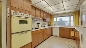 A kitchen with wooden cabinets, a double oven, a sink, and a window with curtains. - Cozy Hillsdale Home ~ 1 Mi to Baw Beese Lake! (Hillsdale)
