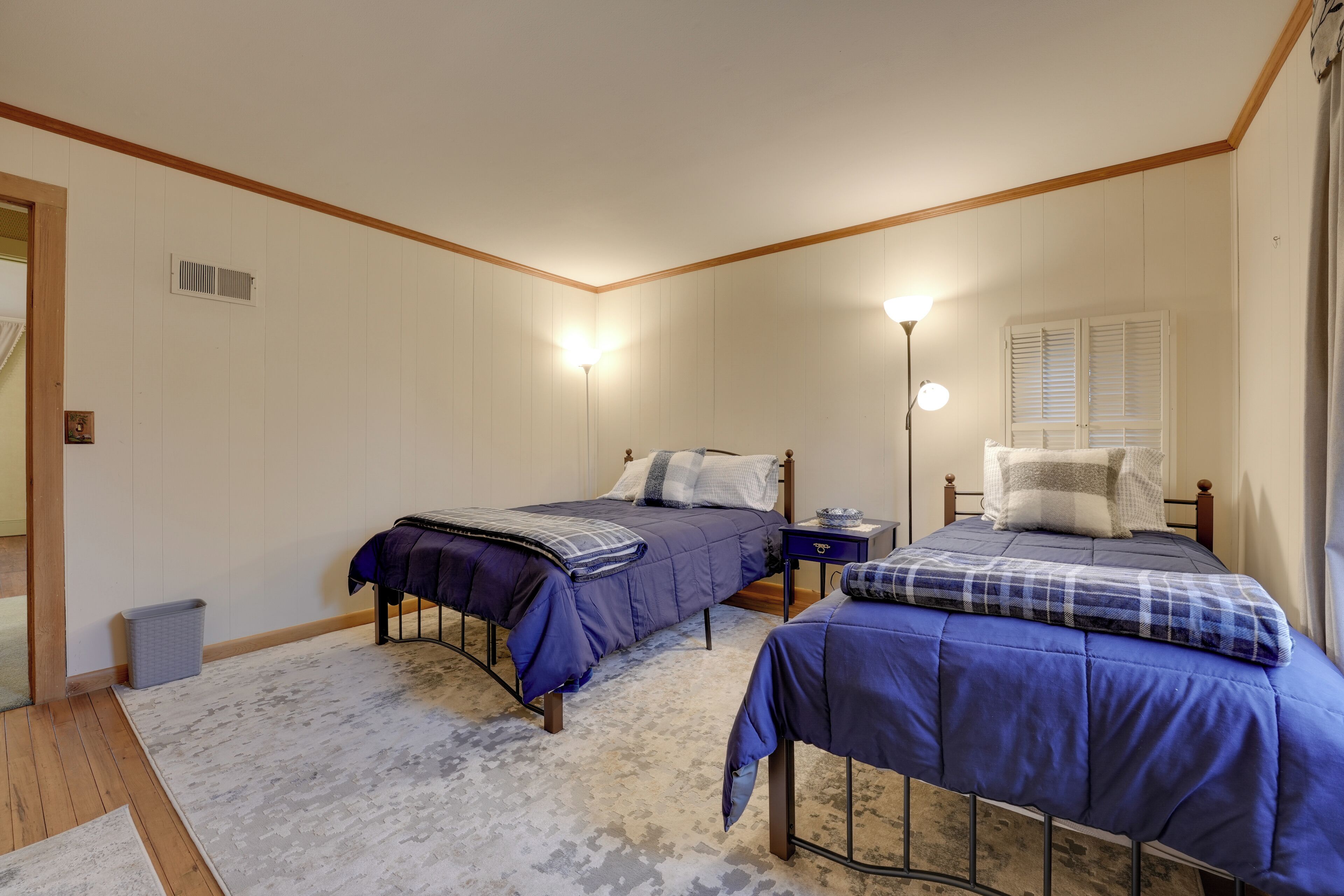 Een slaapkamer met twee bedden, een nachtkastje, een lamp en een raam met shutters.