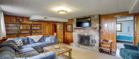 A cozy living room with a stone fireplace, wooden walls, and a large sectional sofa.