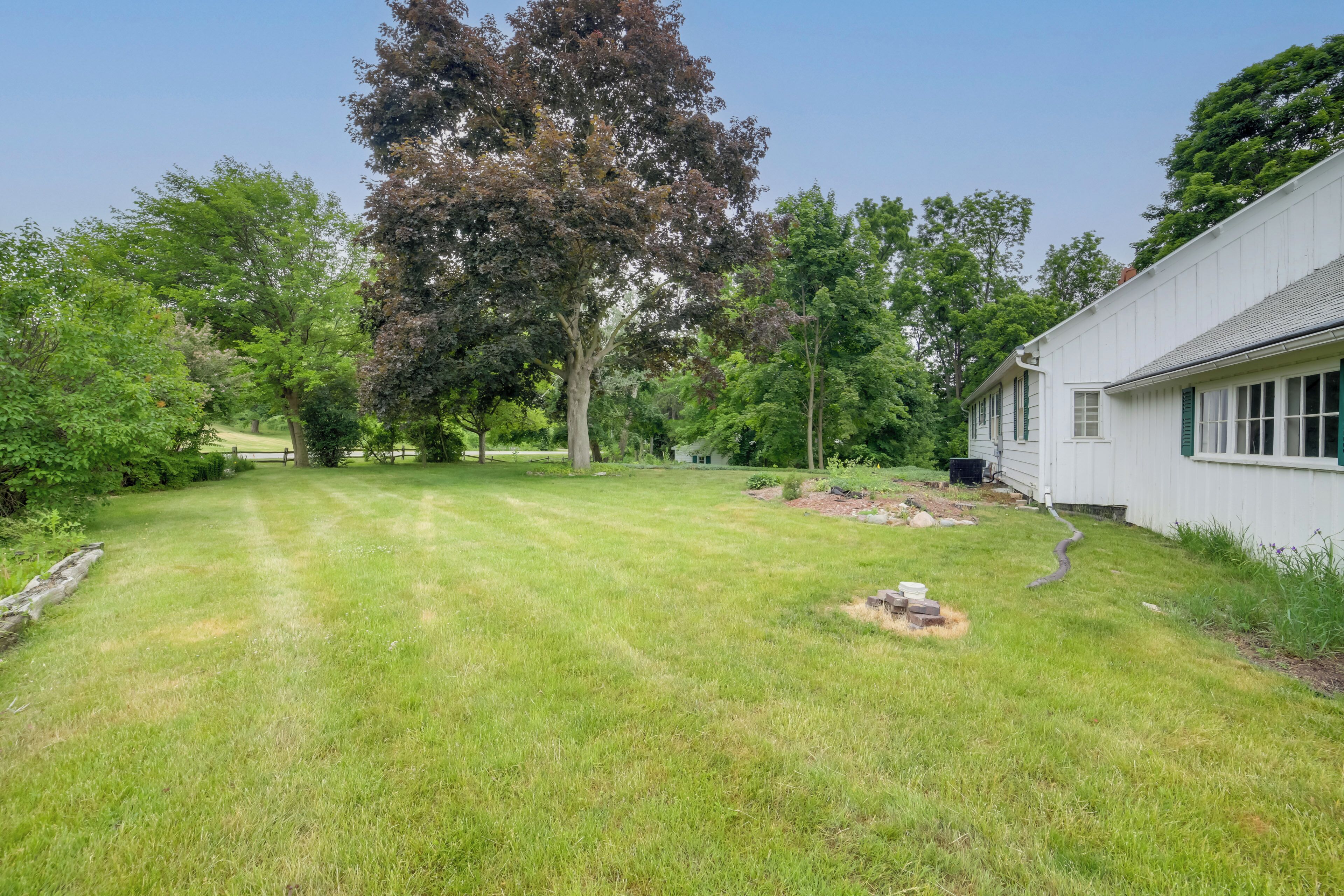 A well-maintained lawn with a large tree and a white building with green shutters.