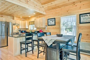 A wooden cabin interior with a kitchen, dining area, and a framed map on the wall. - Maine Cabin Rental on Rangeley Lake! (Rangeley)