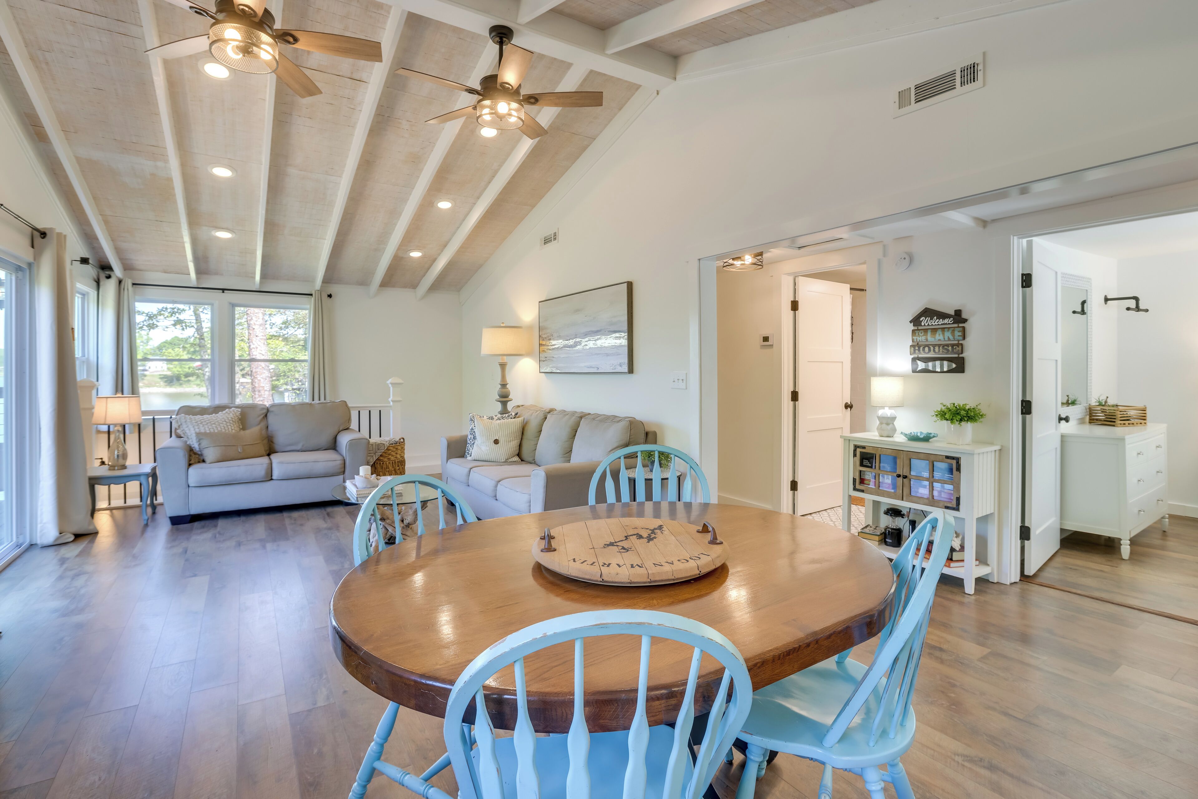 A spacious living room with a large wooden dining table surrounded by blue chairs, a sofa, and a lamp.