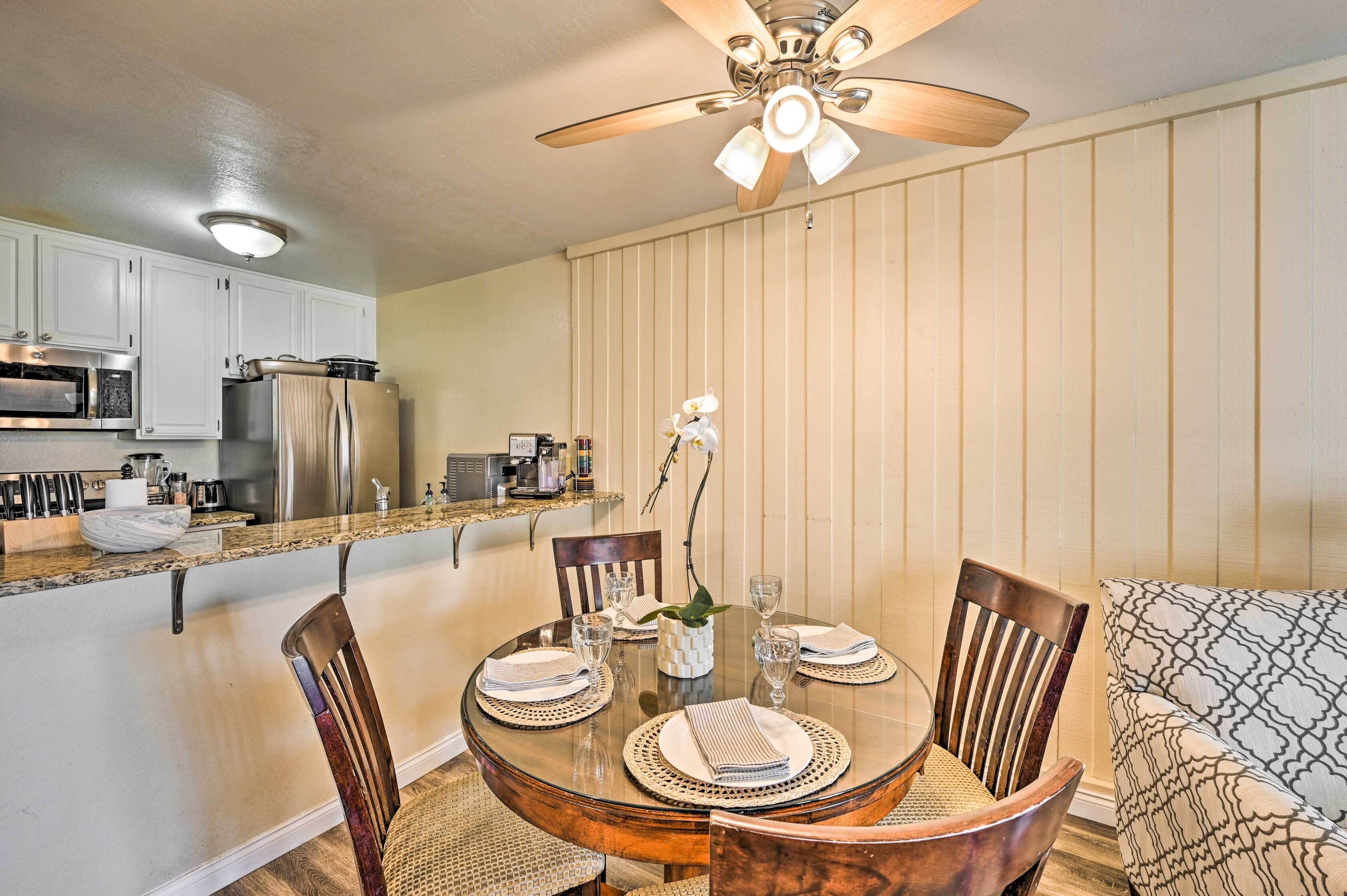 A compact kitchen with white cabinets, a microwave, and a refrigerator. A dining table with chairs and a ceiling fan above is also visible.