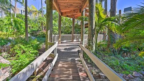 A wooden walkway with railings, surrounded by lush greenery and palm trees. - 'deja Blue' Oceanside Condo on Beach w/ Pools! (Oceanside)