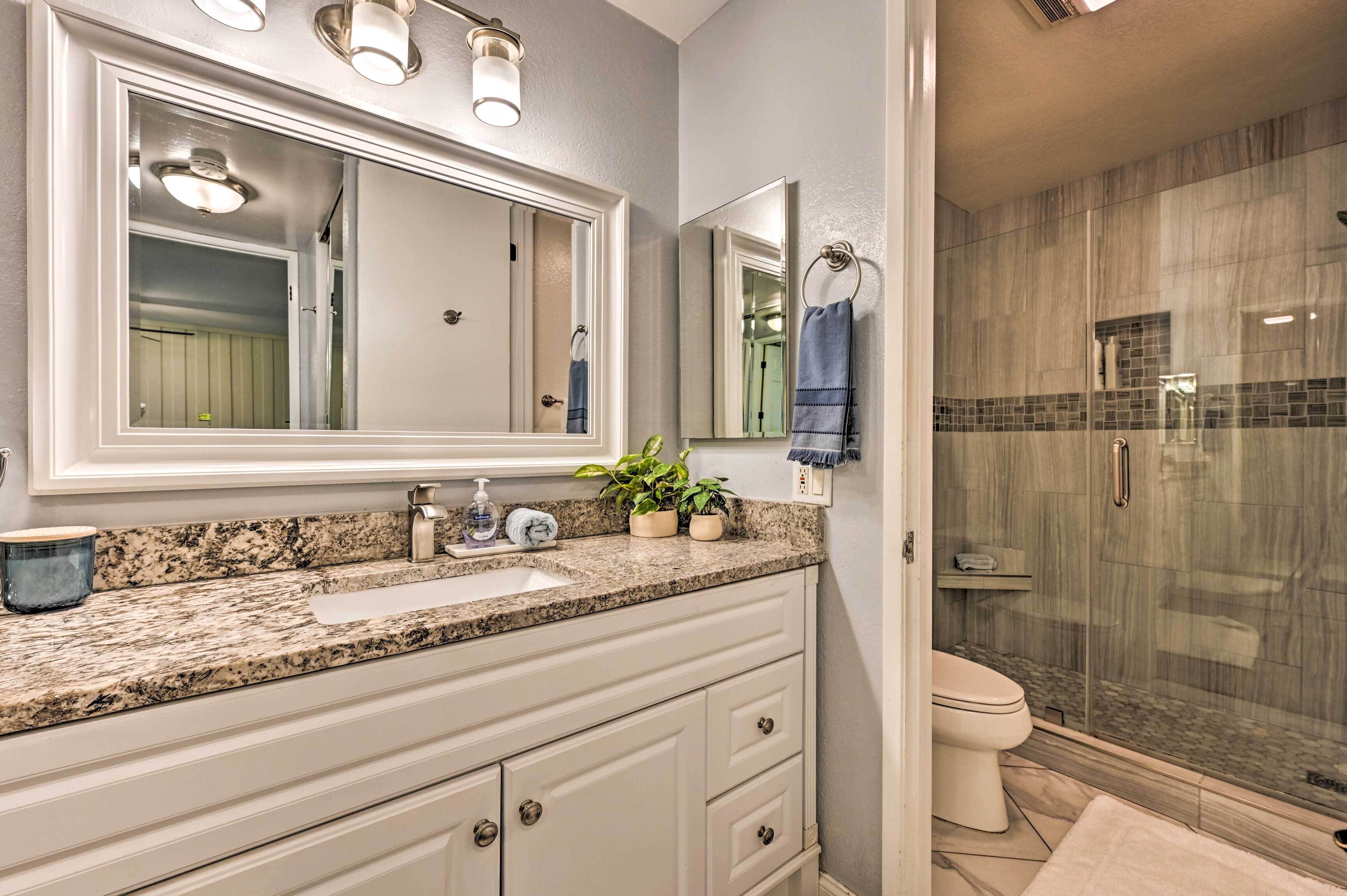 A bathroom with a granite countertop, a large mirror, a sink, a toilet, and a glass-enclosed shower.