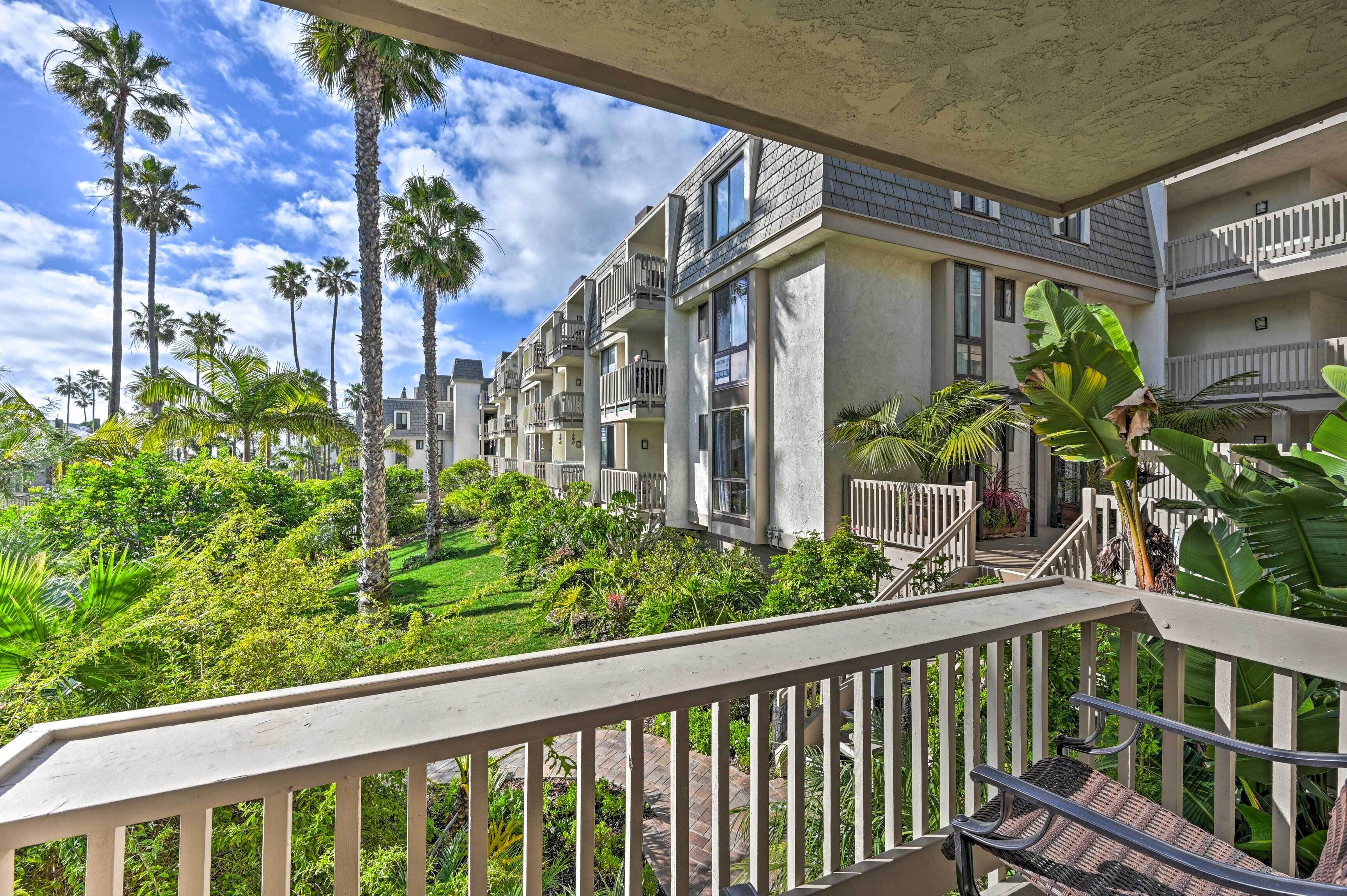 A multi-story residential building with balconies, surrounded by lush greenery and palm trees.