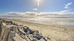A beach with a rocky breakwater and a pier in the background. - 'deja Blue' Oceanside Condo on Beach w/ Pools! (Oceanside)