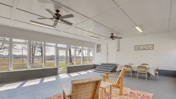 A spacious room with large windows, ceiling fans, a wooden chair, a small table, and a sign that reads "Welcome to Our Place". - Charming Gadsden Home w/ Golf Course Views! (Gadsden)