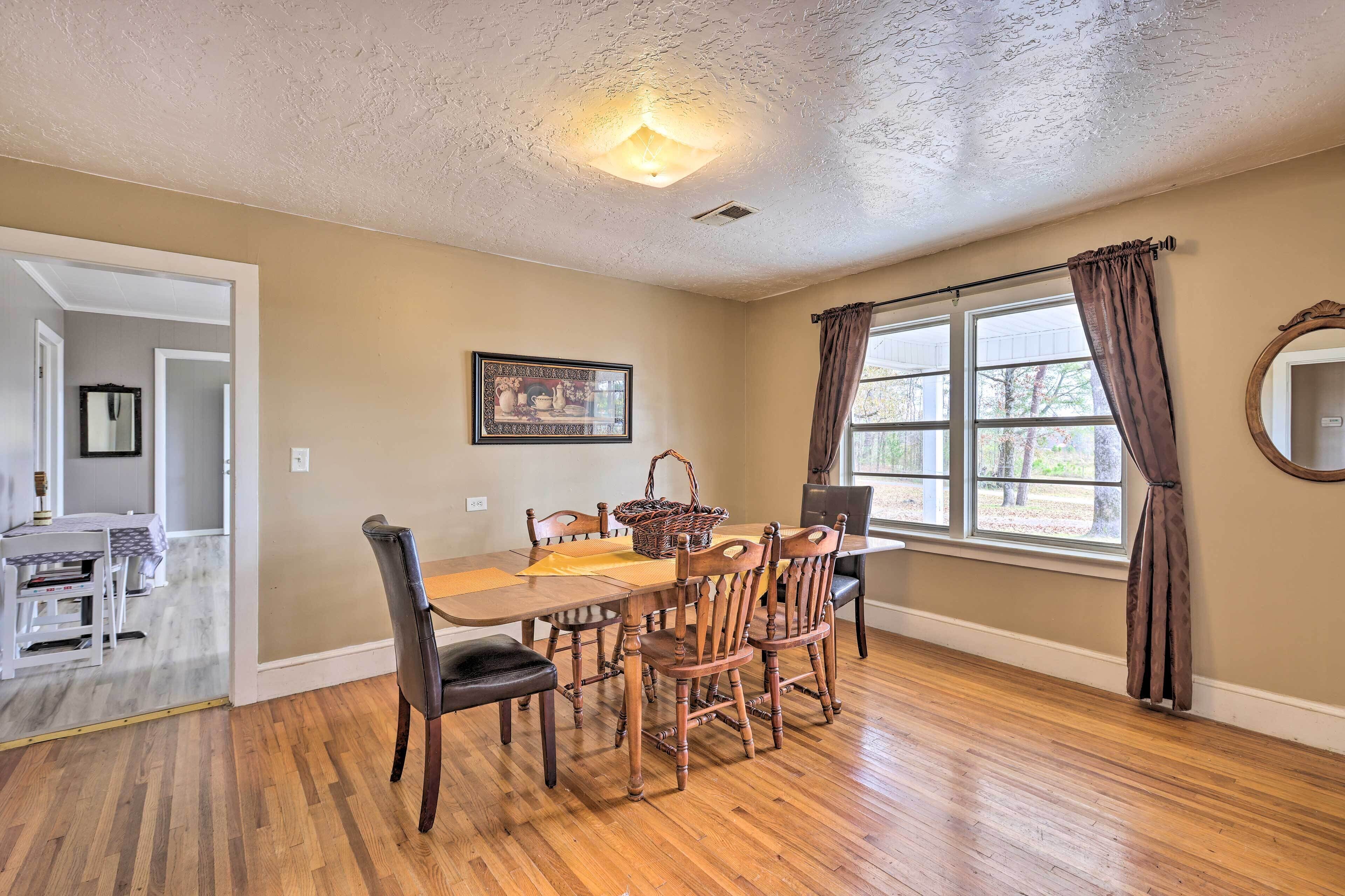 A dining area with a wooden table and chairs, a ceiling light, and a window with curtains.