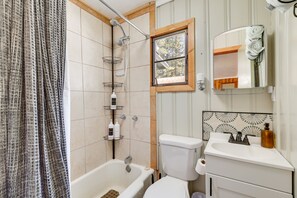 A bathroom with a bathtub, toilet, and sink. There is a window with a view of trees, and a shower with a towel rack. - Pet-friendly Alpine Cabin w/ Gas Grill & Fireplace (Alpine)