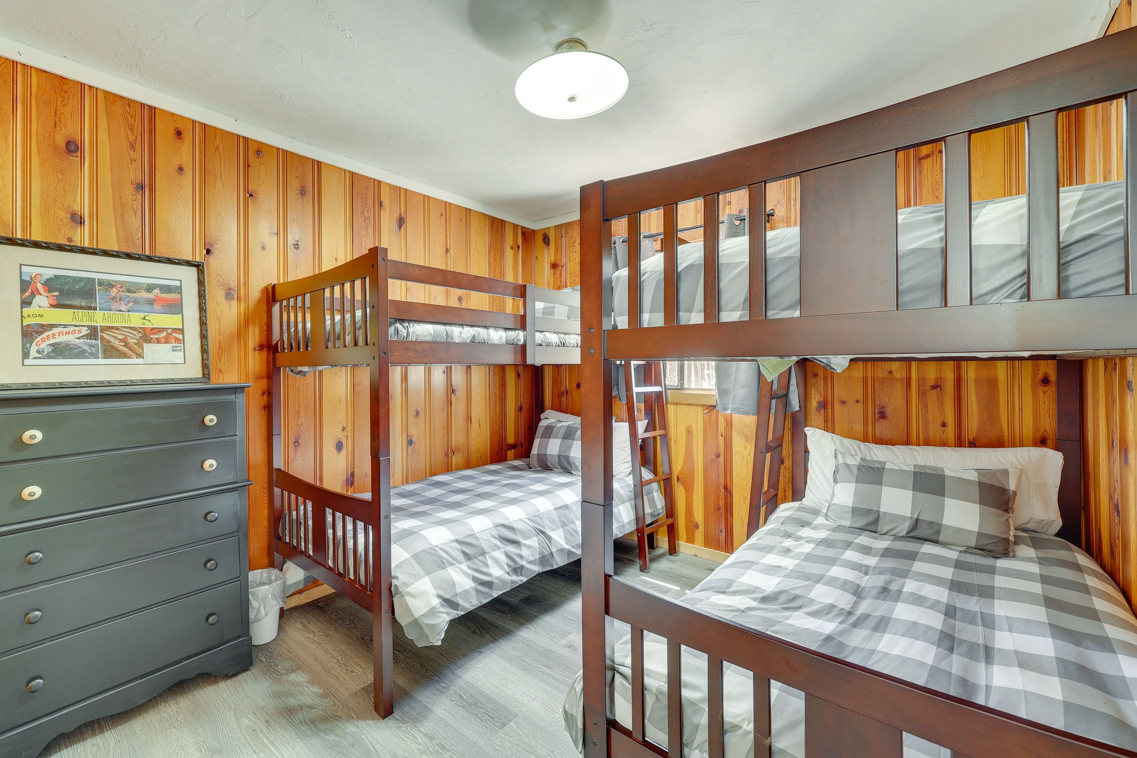 A bunk bed room with wooden walls, a dresser, and a framed picture on the wall.