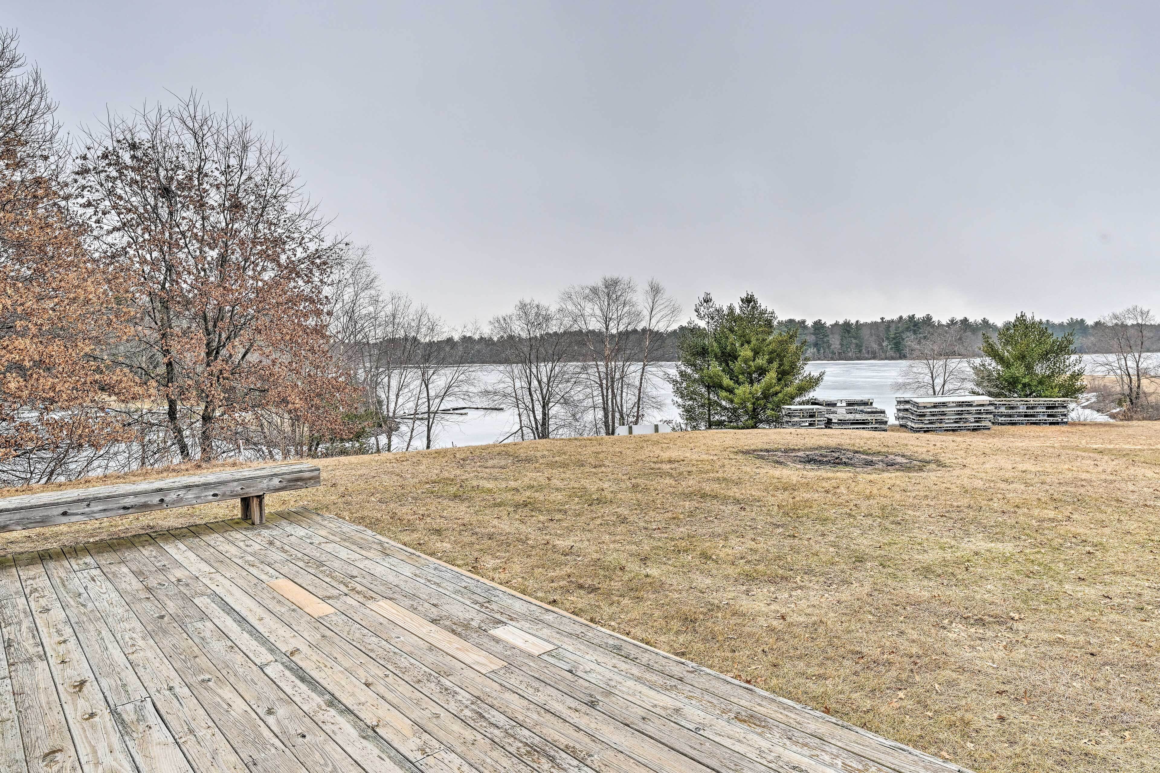 A wooden deck with a bench overlooking a lake, surrounded by trees and a grassy area.