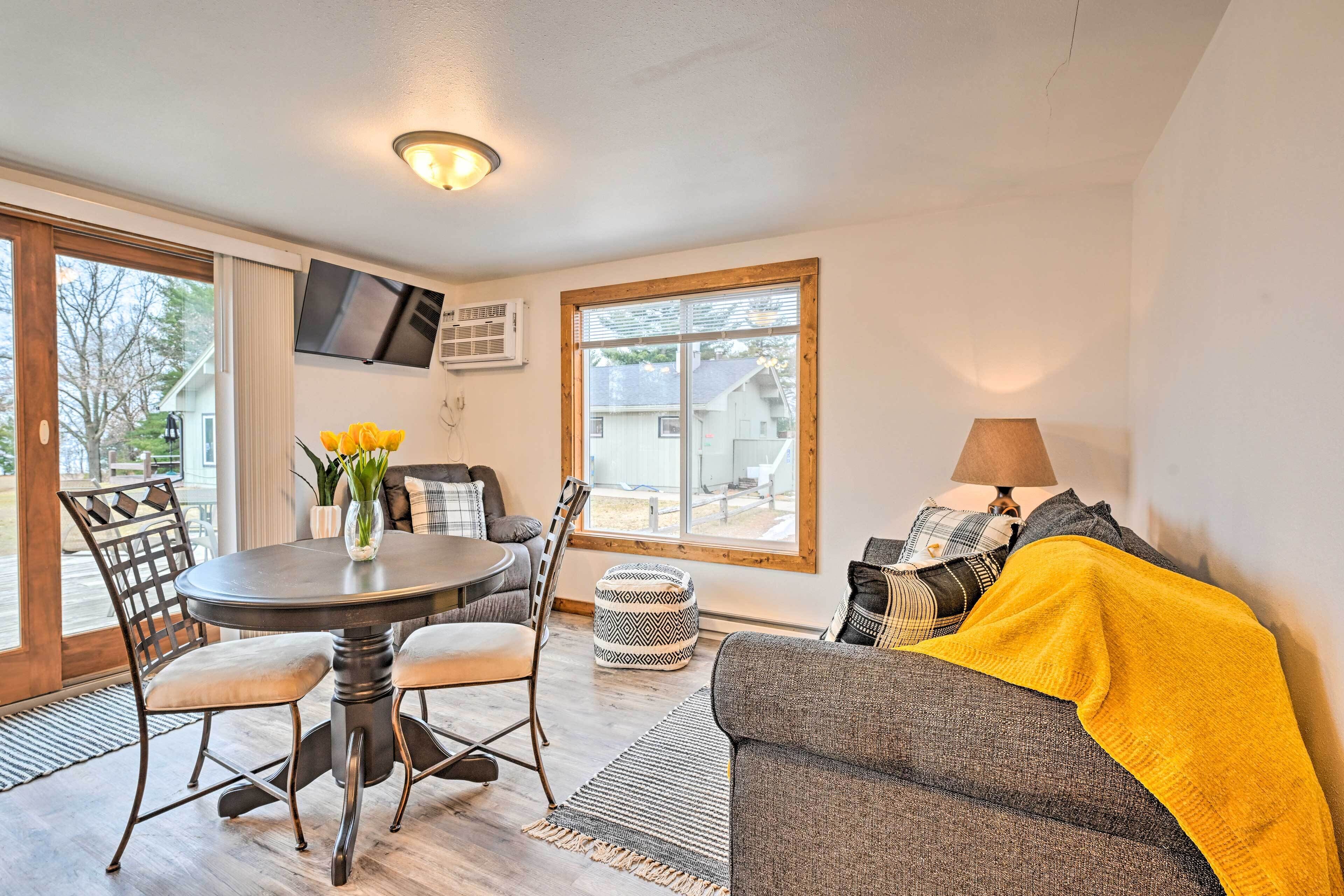 A cozy living area with a round table, chairs, a sofa, and a TV mounted on the wall.