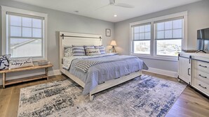 Ein Schlafzimmer mit einem Bett, einer Bank, einem Nachttisch, einer Lampe und Blick durch große Fenster.
