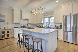 A modern kitchen with white cabinetry, a large island with stools, stainless steel appliances, and a pendant light. - Long Branch Home < 1 Mi to Beach! (Long Branch)