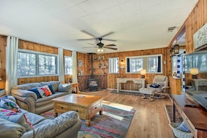 L’intérieur d’un chalet chaleureux, avec une cheminée, des murs en bois et un ventilateur de plafond.