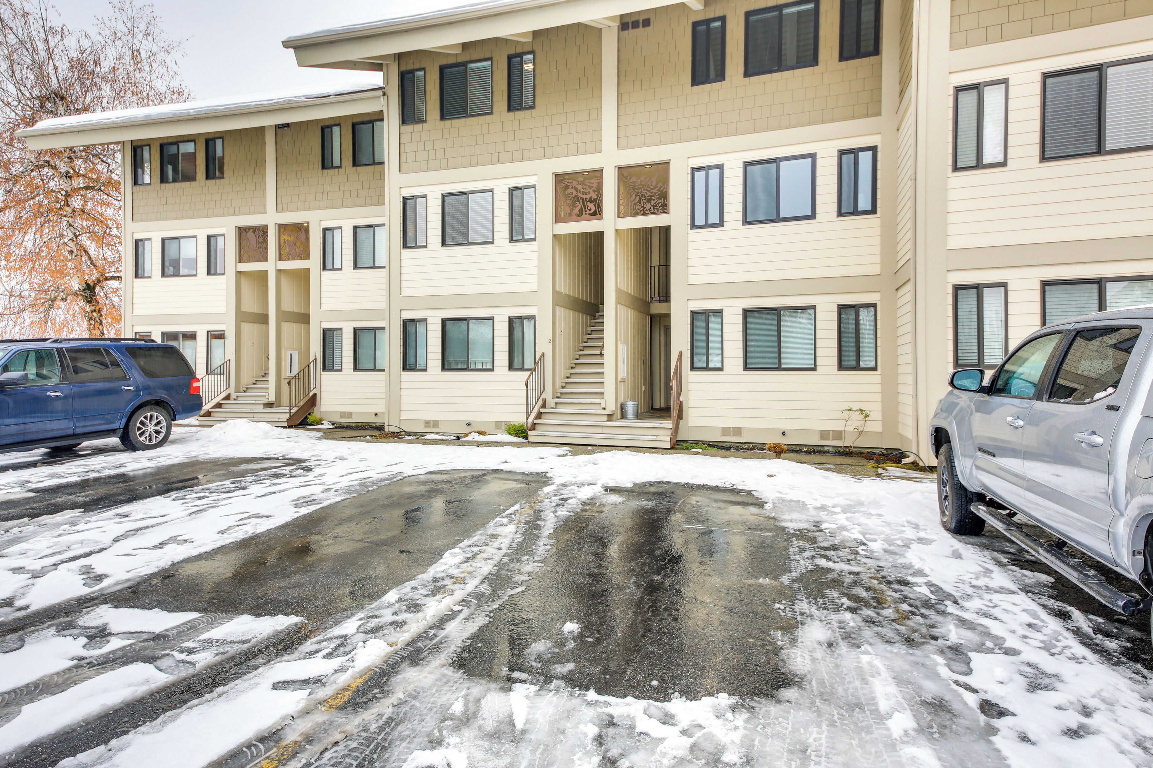 A multi-story building with a central staircase, a parking area with two cars, and a snow-covered ground.